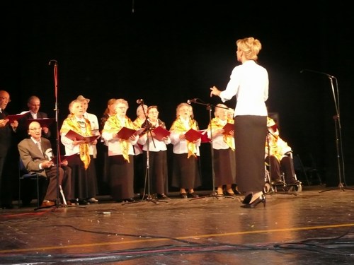 Chór seniorów występuje na scenie, prowadzony przez dyrygentkę