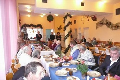 Wigilia 2009 w DPS, seniorzy przy odświętnie udekorowanych stołach, w tle choinka i świąteczne dekoracje